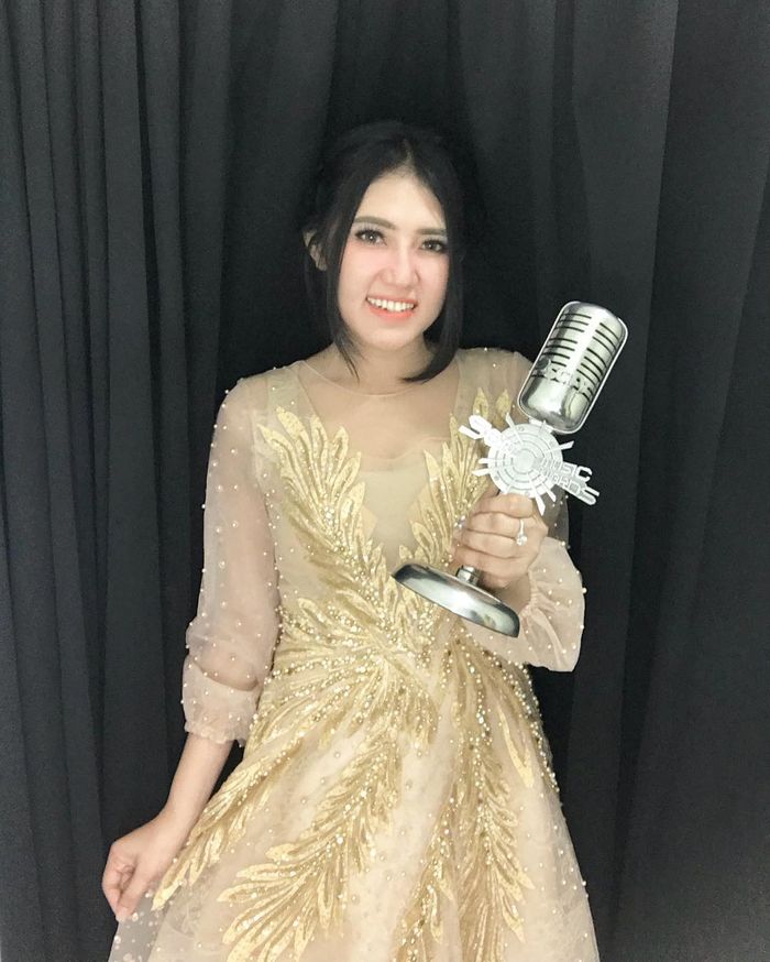 Via Vallen tampil dengan balutan semi sheer dress emas sambil memegang piala