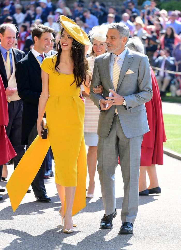 Amal Clooney mengenakan busana cerah berwarna kuning.