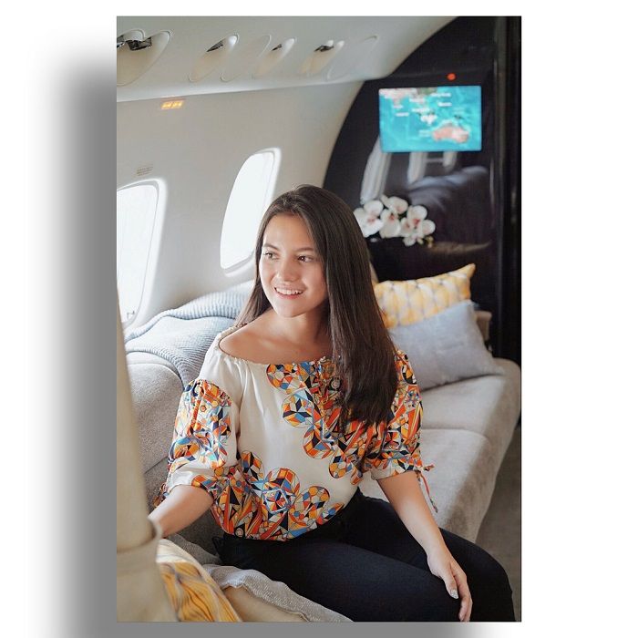 Marsha Aruan saat berlibur bersama Maia Estianty menggunakan jet pribadi, berpose di atas sofa bernuansa abu-abu.