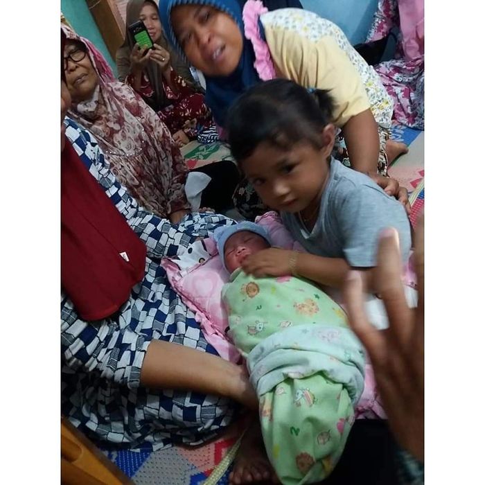 Anak perempuan Erni dan Romi menggendong bayi yang dilahirkan Erni