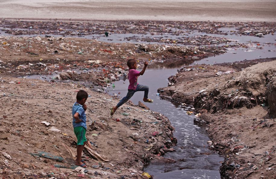 Seorang anak melompati selokan yang dikelilingi sampah di Kanpur, India
