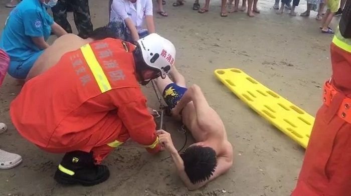 Seeorang petugas pemadan kebakaran sedang membantu mengeluarkan ekor ikan pari dari dalam celana seorang laki-laki