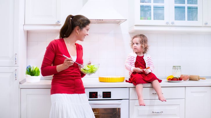 Mother and child bake a pie. Young woman and her daughter cook in a white kitchen. Kids baking pastry. Children helping to make dinner. Modern interior with oven and other appliances. Family eating.