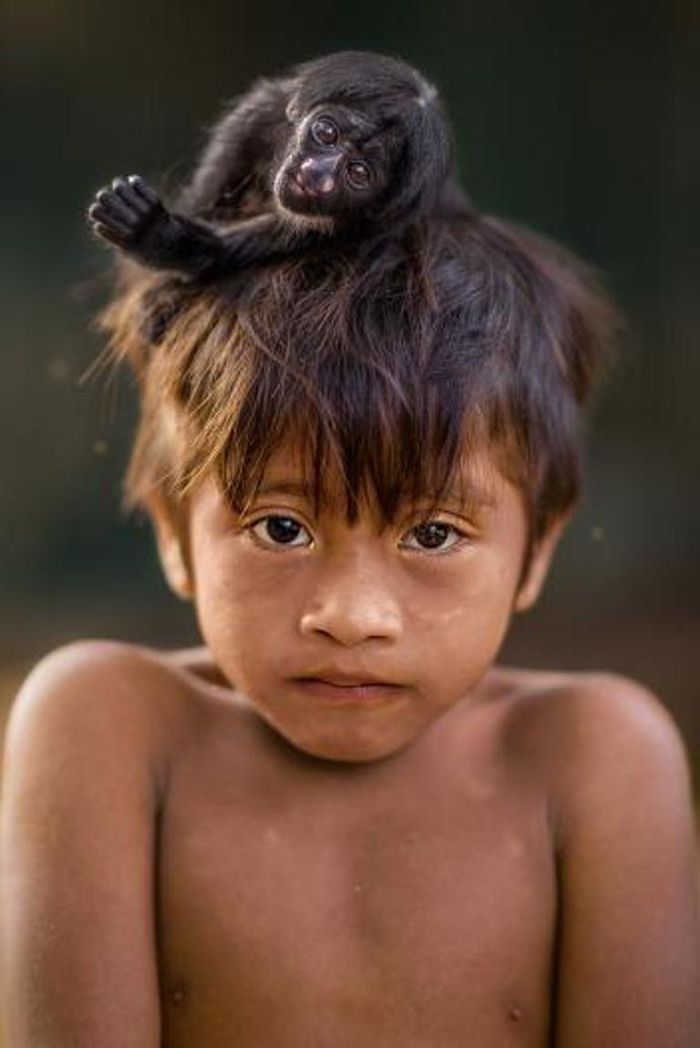 Potret seorang anak dari suku Awa dengan monyet di kepalanya.