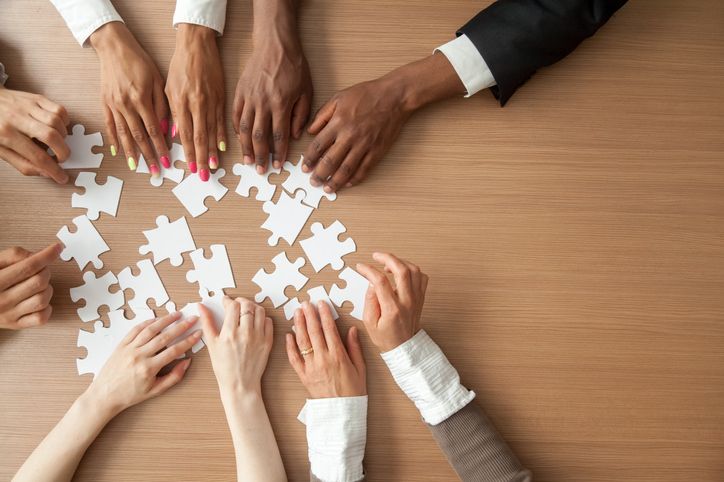 Hands of multi-ethnic team assembling jigsaw puzzle, multiracial group of black and white people joining pieces at desk, successful teamwork concept, help and support in business, close up top view