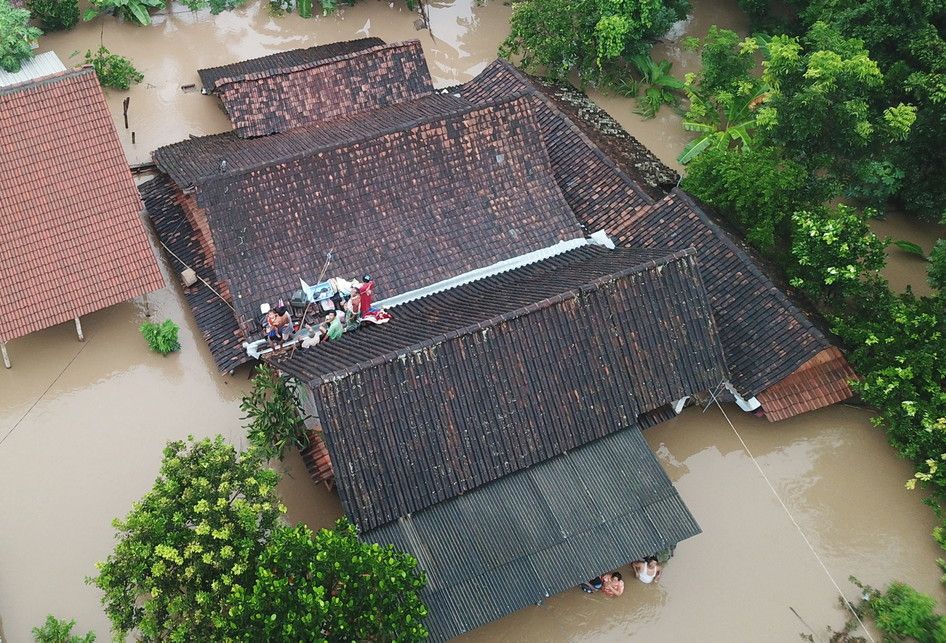 Sejumlah warga menyelamatkan diri di atas atap rumah saat terjadi banjir di Desa Purworejo, Pilangkenceng, Kabupaten Madiun,  Jawa Timur, Rabu (6/3/2019). Sejumlah anak Sungai Madiun meluap dan merendam sejumlah desa di wilayah tersebut, sehingga ratusan warga yang terjebak banjir harus dievakuasi k