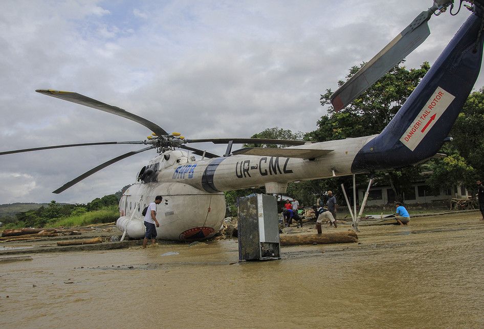 Sejumlah warga berada di dekat helikopter yang bergeser dari tempatnya akibat banjir bandang di Sentani, Kabupaten Jayapura, Papua, Minggu (17/3/2019). Jumlah korban bencana banjir bandang yang terjadi pada Sabtu (16/3/2019) malam kemarin, hingga data yang masuk pada Minggu sore, terus bertambah men