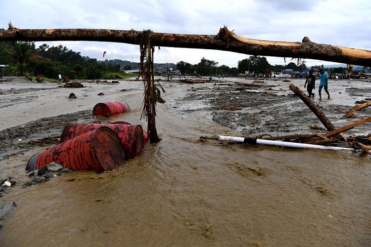 Warga melintasi endapan lumpur pasca banjir bandang melanda wilayah Sentani, Jaya Pura, Papua, Senin (18/3/2019). Akibat banjir bandang yang melanda Sentani sejak Sabtu (16/3) lalu, sedikitnya empat ribu warga mengungsi di sejumlah posko pengungsian. 