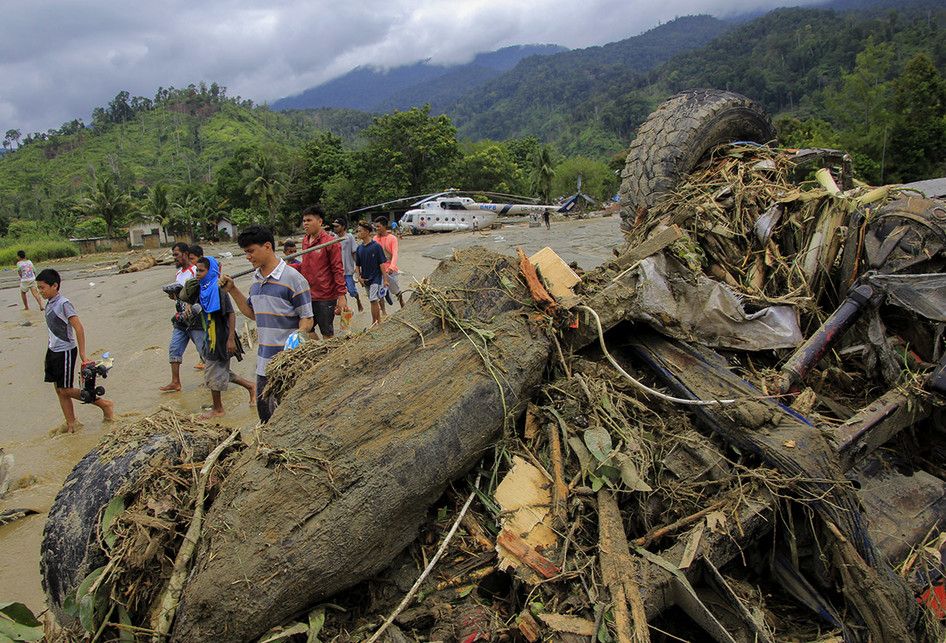 Sejumlah warga melintasi sebuah mobil yang terbalik akibat banjir bandang di Sentani, Kabupaten Jayapura, Papua, Minggu (17/3/2019). Jumlah korban bencana banjir bandang yang terjadi pada Sabtu (16/3/2019) malam kemarin, hingga data yang masuk pada Minggu sore, terus bertambah menjadi 63 orang.