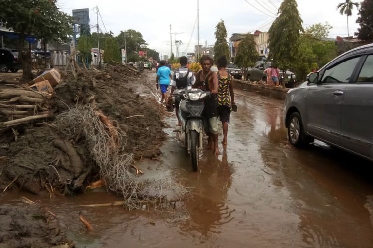 Warga mendorong motor melintasi sisa lumpur akibat banjir bandang di Sentani, Kabupaten Jayapura, Papua, Minggu (17/3/2019). Berdasarkan data BNPB, banjir bandang yang terjadi pada Sabtu (16/3) tersebut mengakibatkan 42 orang tewas.  