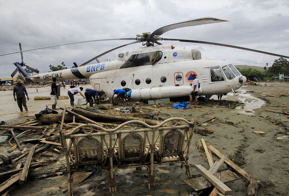 Sejumlah warga berada di dekat helikopter yang bergeser dari tempatnya akibat banjir bandang di Sentani, Kabupaten Jayapura, Papua, Minggu (17/3/2019). Jumlah korban bencana banjir bandang yang terjadi pada Sabtu (16/3/2019) malam kemarin, hingga data yang masuk pada Minggu sore, terus bertambah men