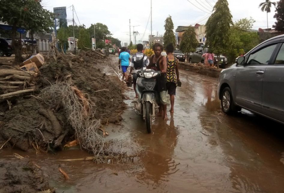 Warga mendorong motor melintasi sisa lumpur akibat banjir bandang di Sentani, Kabupaten Jayapura, Papua, Minggu (17/3/2019). Jumlah korban bencana banjir bandang yang terjadi pada Sabtu (16/3/2019) malam kemarin, hingga data yang masuk pada Minggu sore, terus bertambah menjadi 63 orang.