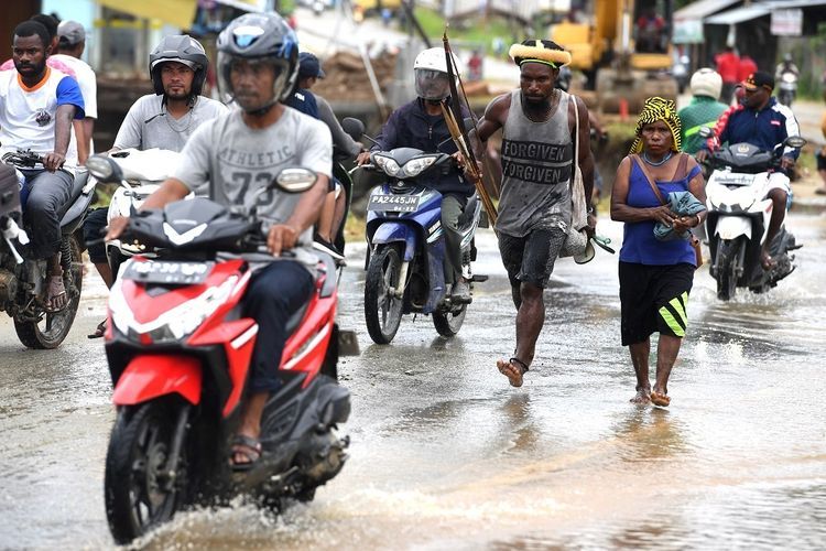 Warga dengan peralatan berburu melintasi genangan air pasca banjir bandang melanda wilayah Sentani, Jaya Pura, Papua, Senin (18/3/2019). Akibat banjir bandang yang melanda Sentani sejak Sabtu (16/3) lalu, sedikitnya empat ribu warga mengungsi di sejumlah posko pengungsian. 