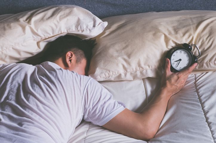 sleeping asian young male disturbed by alarm clock early morning in bed