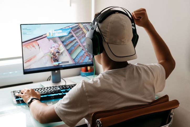 Madrid, Spain - August 15, 2018: Teenager playing Fortnite video game on PC. He is raising his fist in a victory gesture. Fortnite is an online multiplayer video game developed by Epic Games