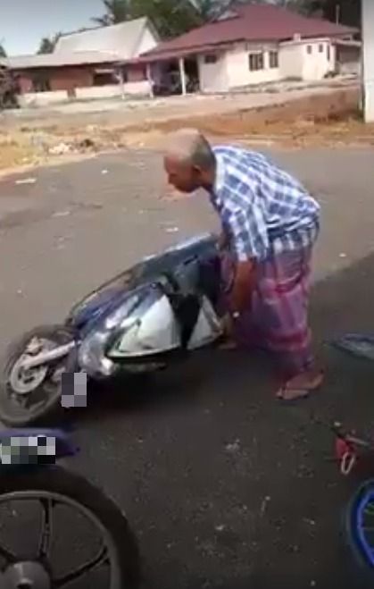 Pria tua mencoba mengangkat sepeda motornya. 