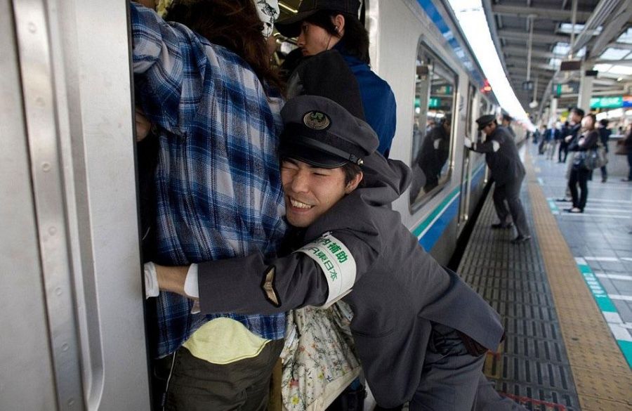 Petugas kereta di Jepang mendorong penumpang ke dalam kereta yang penuh