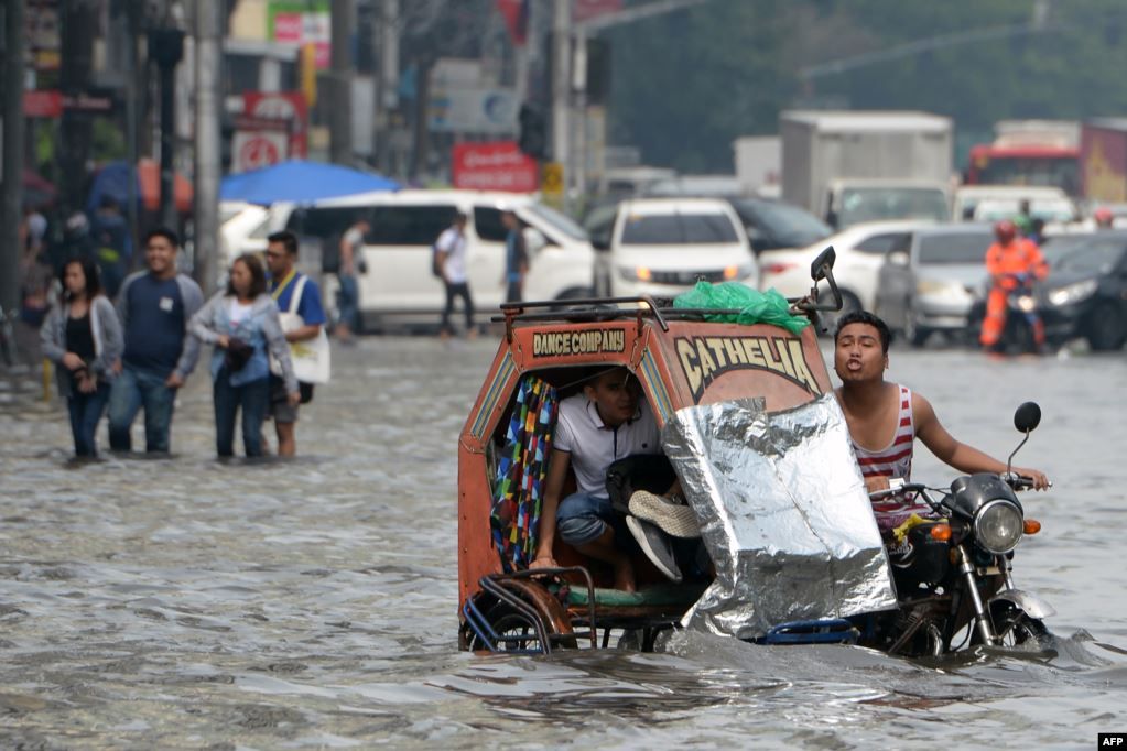 Seorang penumpang melepas sepatunya saat naik kendaraan semacam betor (becak motor), melalui jalan yang tergenang banjir, akibat hujan lebat yang melanda Manila, Filipina.