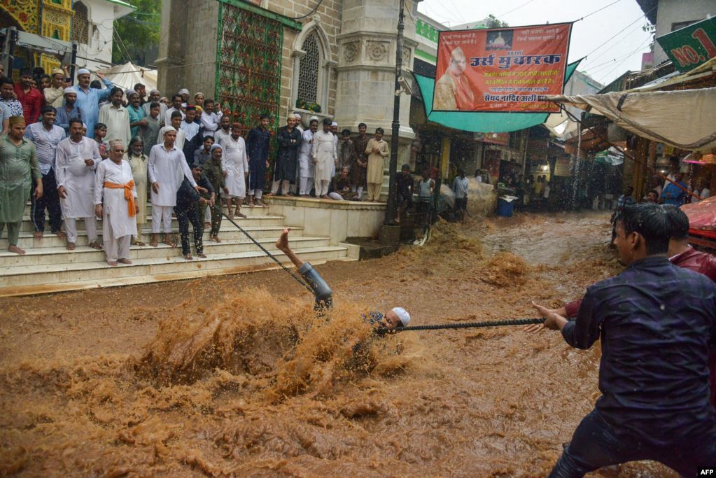 Seorang pria terjatuh ketika mencoba memegang tali untuk membantu orang menyeberangi jalan yang tergenang banjir setelah hujan lebat di luar kuil sufi Moinuddin Chishti di kota Ajmer, negara bagian Rajasthan, India barat, Kamis (1/8).