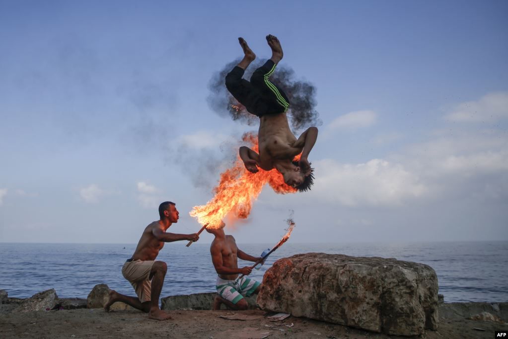 Pria Palestina melakukan atraksi di pantai dengan menyemburkan api dari mulutnya, sebagai hiburan bagi anak-anak selama liburan musim panas di kota Gaza 1 Agustus 2019.