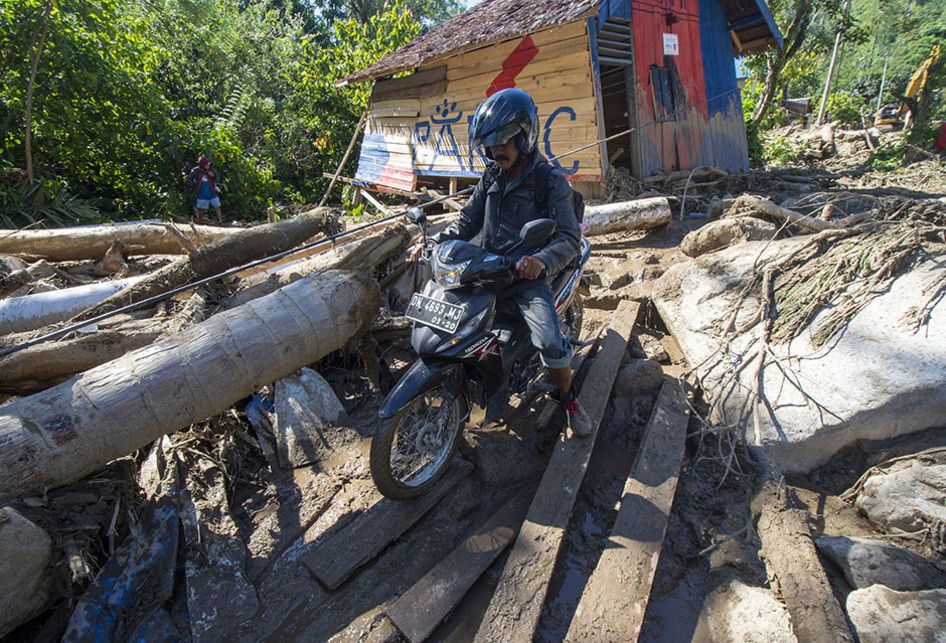 Warga mengendarai sepeda motor berusaha melewati jalan yang dipenuhi lumpur, bebatuan serta material lainnya pascabanjir bandang di Desa Namo, Kecamatan Kulawi, Kabupaten Sigi, Sulawesi Tengah, Rabu (14/8/2019). Banjir bandang yang menerjang wilayah itu pada Selasa (13/8/2019) malam mengakibatkan pu