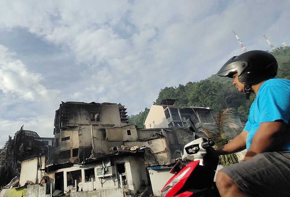 Seorang warga melintasi puing bangunan yang terbakar seusai aksi unjuk rasa di Jayapura, Papua, Jumat (30/8/2019). Sejumlah bangunan dan kendaraan terbakar saat aksi unjuk rasa yang berakhir rusuh di Jayapura, Kamis kemarin, masih terkait memprotes dugaan tindak rasisme kepada mahasiswa Papua di Jaw