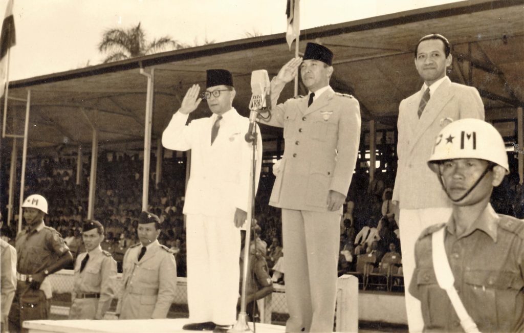 Presiden Soekarno (tengah) dan Wakil Presiden Mohammad Hatta (kiri) membuka Pekan Olahraga Angkatan Perang di Stadion Ikada Jakarta, September 1952. Hadir di panggung kehormatan Menteri Pertahanan Hamengku Buwono IX (kanan).