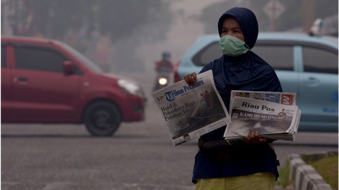 Seorang penjual koran mengenakan masker saat berjualan di tengah asap kebakaran hutan dan lahan (Karhutla) yang makin pekat menyelimuti Kota Pekanbaru, Riau, Jumat (13/9). 