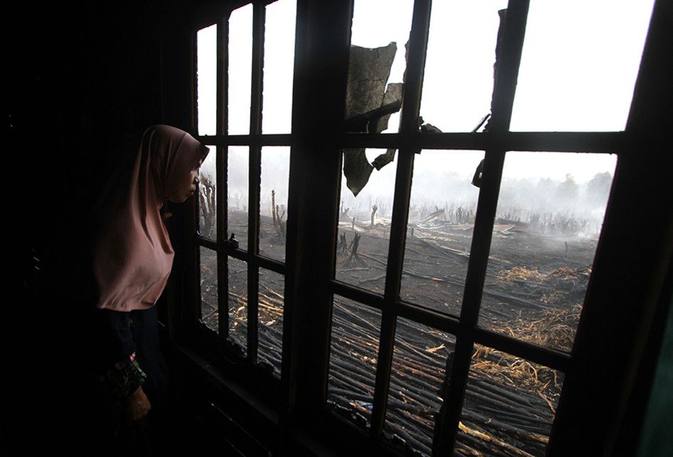 Warga melihat kebakaran lahan gambut dari balik jendela rumah di desa Pengayuan, Banjarbaru, Kalimantan Selatan, Sabtu (14/9/2019). Kebakaran lahan gambut di kawasan tersebut mengakibatkan satu tempat usaha warga dan sebagian dinding rumah warga ikut terbakar.