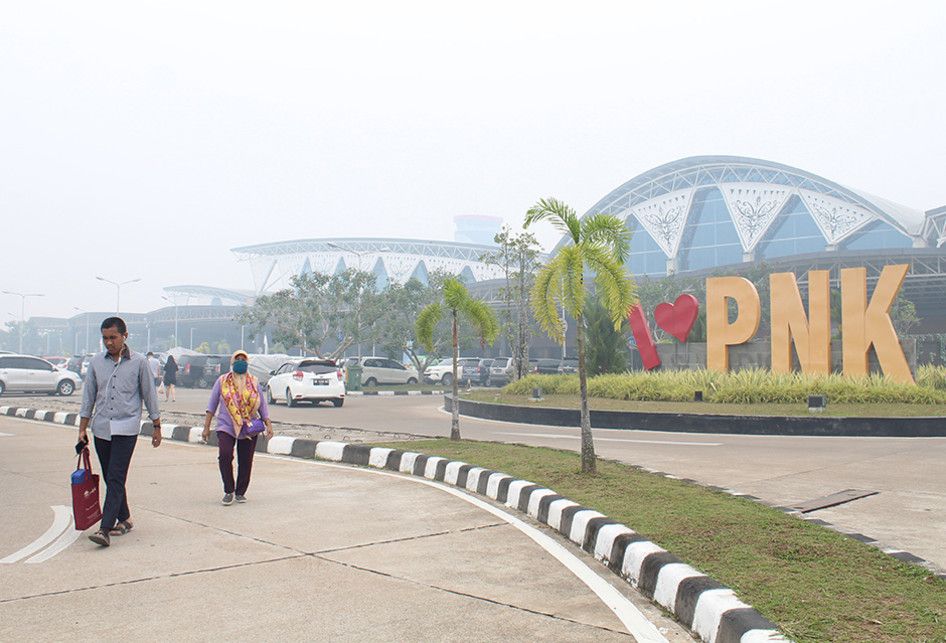 Warga berjalan di kompleks Bandara Supadio yang diselimuti kabut asap di Kabupaten Kubu Raya, Kalimantan Barat, Minggu (15/9/2019). Plt Kadiv Operasional Bandara Internasional Supadio Pontianak Andry Felanie menyatakan bahwa pada Minggu (15/9/2019) terdapat 19 penerbangan keberangkatan dan 18 penerb