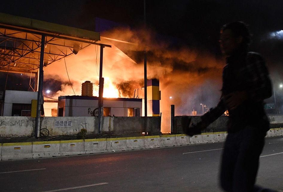 Warga melintasi Gerbang Tol Pejompongan yang dibakar massa, di Jakarta, Selasa (24/9/2019). Demo mahasiswa yang berlangsung di depan Gedung DPR sejak tadi pagi berakhir ricuh, suasana tidak kondusif terjadi sejak sore hingga malam hari.