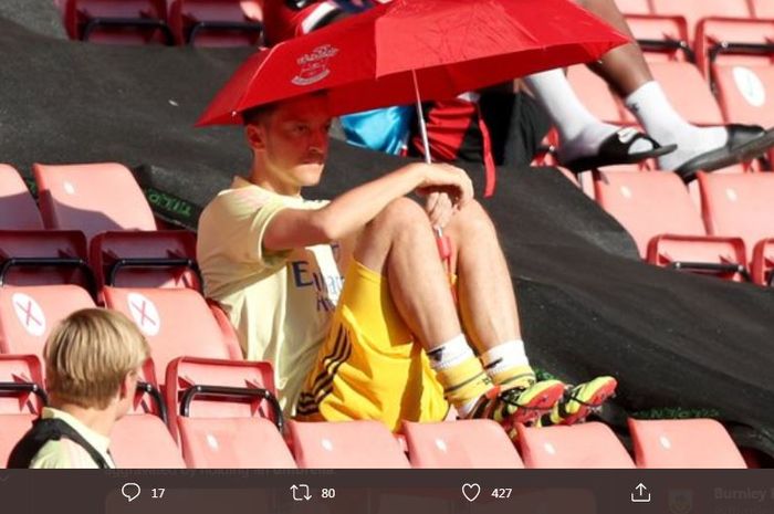 Mesut Oezil menyaksikan laga Arsenal dari bangku penonton dengan memakai payung.