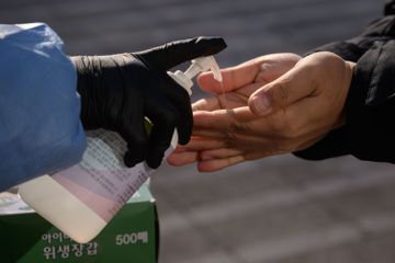 Seorang petugas kesehatan memberikan hand sanitizer sebelum orang-orang melakukan tes untuk virus corona baru di pusat pengujian sementara di alun-alun balai kota di Seoul . pada 18 Desember 2020. (Foto AFP)