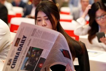 Seorang perempuan membaca media cetak terbitan negara China.