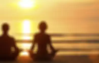 Young couple practicing yoga on the beach at sunset.
