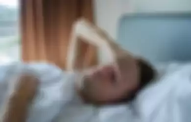 Caucasian man lying in bed at home suffering from headache or hangover. Concept of problem with health.