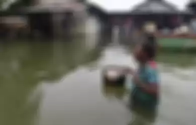 Seorang warga menerobos banjir yang melanda permukiman mereka di dekat Danau Sentani, Sentani, Jayapura, Papua, Selasa (19/3/2019). Akibat banjir bandang yang melanda Sentani sejak Sabtu (16/3) lalu, jumlah warga yang mengungsi ke sejumlah posko pengungsian bertambah menjadi sedikitnya enam ribu ora
