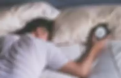 sleeping asian young male disturbed by alarm clock early morning in bed