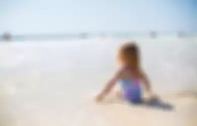 Seorang anak kecil berjemur di pantai.