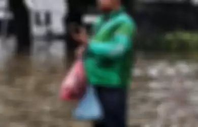 Yudhi Ammaral, seorang pengemudi ojek online Grab mengantarkan pesanan di tengah banjir Jakarta, Sabtu (20/2/2021). 