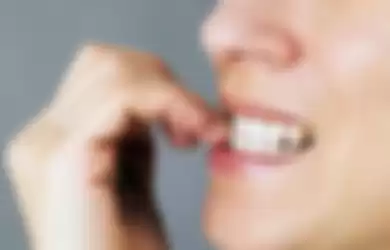 Nervous young woman biting her nails on gray background
