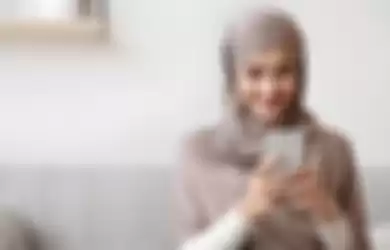 Ilustrasi wanita muslim sedang menunggu waktu buka puasa (ngabuburit) dengan bermain smartphone di Ramdan 2023. 