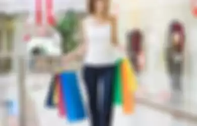 Wanita yang tengah berjalan kaki di mall sembari menenteng tas belanjaannya