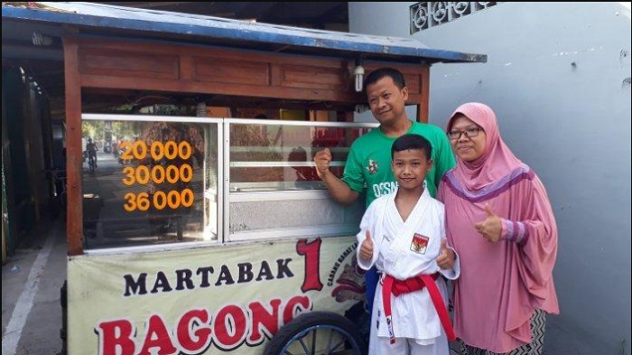 Nandana Putra Purnama bersama kedua orang tuanya, Rohman Sidik Purnomo dan Nuryani Puji Lestari berdiri di depan gerobak martabaknya, Solo, Sabtu (2/12/2018)