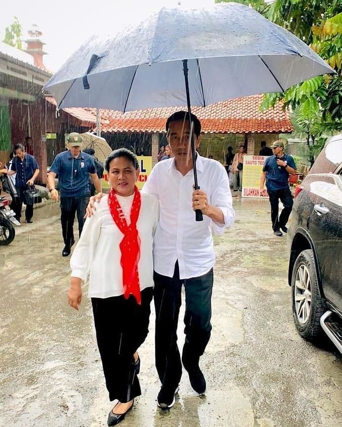 Presiden Joko Widodo merangkul Ibu Iriana sambil memayunginya di tengah hujan.
