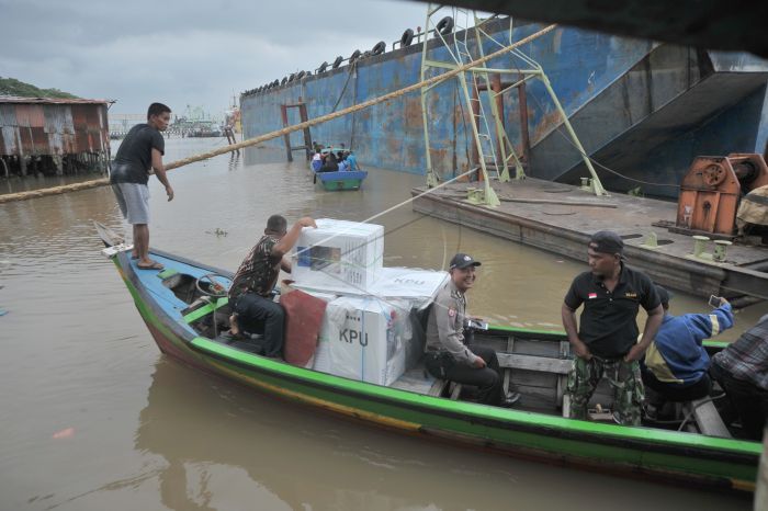Petugas menyeberang sungai dan membawa logistik.