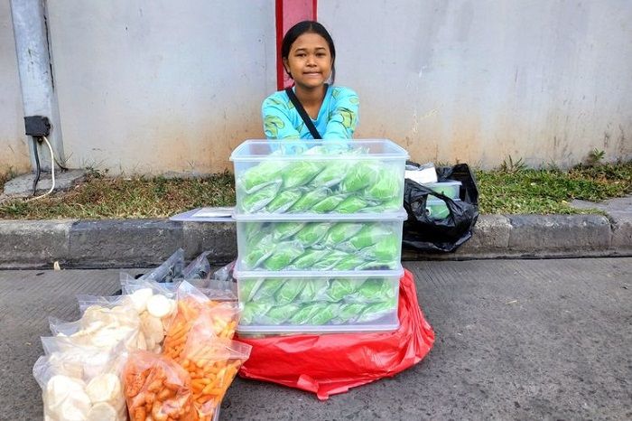 Dewi saat menjajakan bakpao sambil membawa tas berisi buku pelajaran untuk belajar.