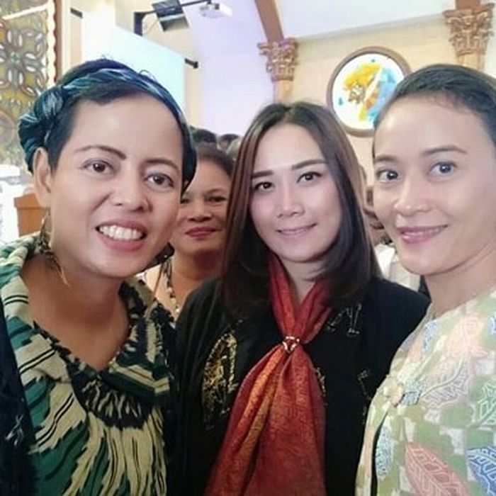 Puput Nastiti Devi tengah mengenakan atasan dengan motif pola dengan gambar pengulangan berwarna emas yang dipadankan dengan syal batik oranye