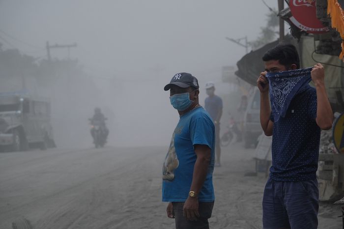 Orang menggunakan masker saat abu vulkanik mulai menebal