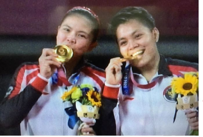 Greysia Polii dan Apriyani Rahayu menggigit medali emas seusai menang atas pasangan China dalam final bulu tangkis ganda putri Olimpiade Tokyo 2020.